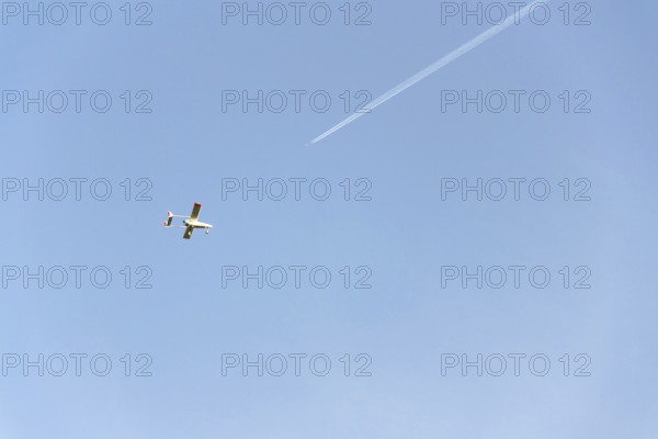 Unmanned aerial vehicle surveillance drone with light and camera flying, sunny summer day, drone delivery concept, copy space on clear sky, condensation trails and airplane in background Pisek Czech republic