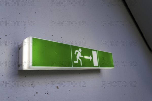 Green shining escape exit sign on white concrete wall