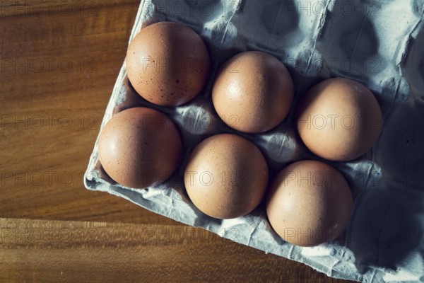 Six brown raw hen eggs on gray tray lying on wooden table, copy space