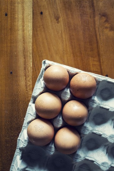 Six brown raw hen eggs on gray tray lying on wooden table, copy space