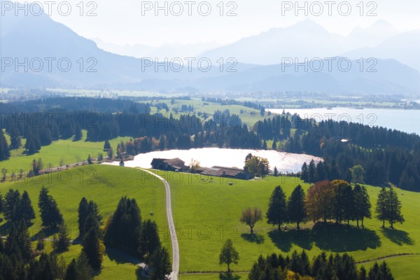 Wide landscape with green areas, Hegratsried Lake and mountains under clear sky, farm, near Füssen, Allgäu, Swabia, Bavaria, Germany