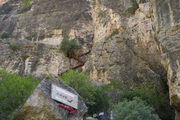 Steep rock wall with a cave and a signpost, Amaghu Gorge, rock wall has a cave with bats to which an iron spiral staircase leads, Vayots Dzor province, Wajoz Dzor, Armenia, Caucasus