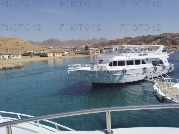 A berth for tourist yachts at the seaport of the resort town of Sharm el-Sheikh. From here, tourists and travelers embark on boat trips offering a variety of leisure and recreational programs, including diving and snorkeling in the Ras Mohammed Marine Reserve and a cruise to the tropical White Island in the crystal-clear turquoise azure waters of the Red Sea. The desert and mountains of the Sinai Peninsula are visible in the background. South Sinai, Sharm el-Sheikh, Egypt