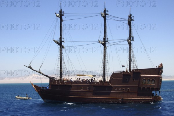 The luxury pirate yacht Black Pearl, with a group of tourists on board, enjoys a cruise through the vast tropical expanses of the Red Sea. The vessel is located near the seaport of the resort town of Sharm el-Sheikh, where tourists and travelers depart for boat excursions. The desert and mountains of the Sinai Peninsula are visible in the background. South Sinai, Sharm el-Sheikh, Egypt
