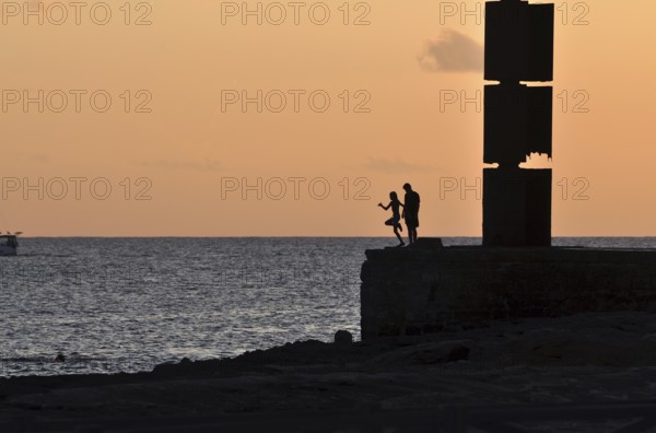 Silhouette of a girl jumping into the sea while a boy is watching, Majorca, balearics, spain