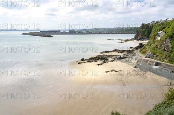 The view over a wide sandy and pebble beach at low tide towards the distinctive Port du Legue breakwater and the port area, while on the right a green coastal slope with isolated buildings slopes down to Anse aux Moines, Plerin, Saint-Brieuc Bay, Cotes-d'Armor, Brittany region, France