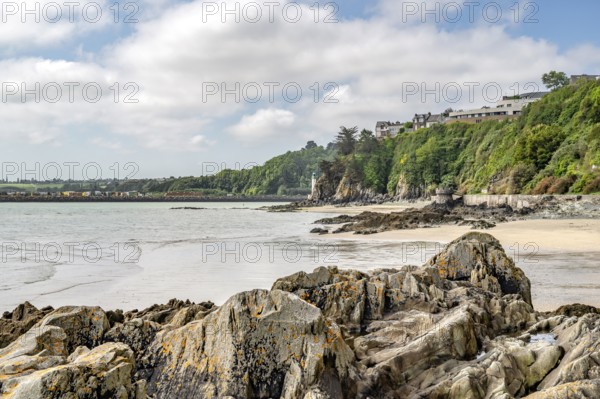 Sharp-edged rocks and sandy beach line Anse aux Moines with its densely overgrown cliff and houses above it in the municipality of Plerin, Saint-Brieuc Bay, Cotes-d'Armor, Brittany region, France
