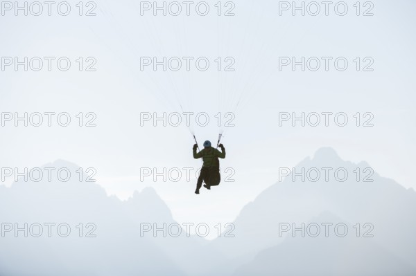 A paraglider floats against a mountain backdrop in morning light, Schwangau, Kostallgäu, Allgäu, Swabia, Bavaria, Germany