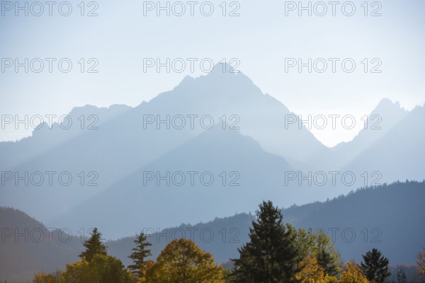The sun shines over a mountain range lined with autumn trees, Schwangau, Ostallgäu, Allgäu, Swabia, Bavaria, Germany