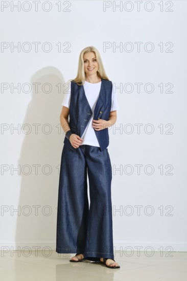 A woman stands confidently in a modern studio dressed in a denim vest and wide-legged pants. The light showcases her relaxed style, perfect for summer outings or casual gatherings