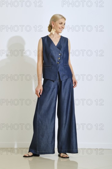 A model is wearing a chic denim vest and wide-legged pants in a well-lit studio. She poses confidently, highlighting her outfit's unique design and texture