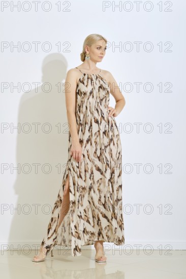 A woman stands confidently wearing a fashionable long dress featuring a unique pattern. She poses gracefully against a plain backdrop, creating a modern and elegant look