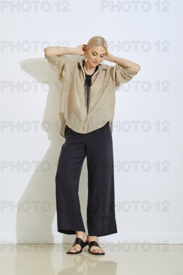 A model showcases a relaxed outfit consisting of a loose beige shirt and dark wide-leg pants