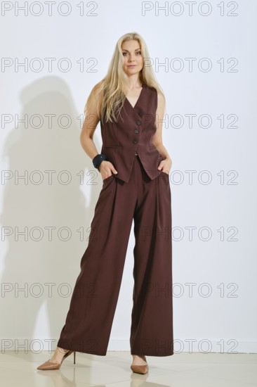 A model stands confidently in a brown vest and matching pants. Her long hair flows down as she poses with a relaxed expression