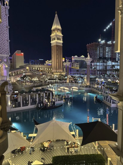 Since the legalization of gambling in the 1930s, Las Vegas has developed as a tourist center of international importance. Where simple casinos initially settled, Las Vegas is now characterized by luxurious hotel complexes with large casinos and leisure facilities, illuminated canal scene at night with distinctive architecture and water tower, Las Vegas, Nevada, USA
