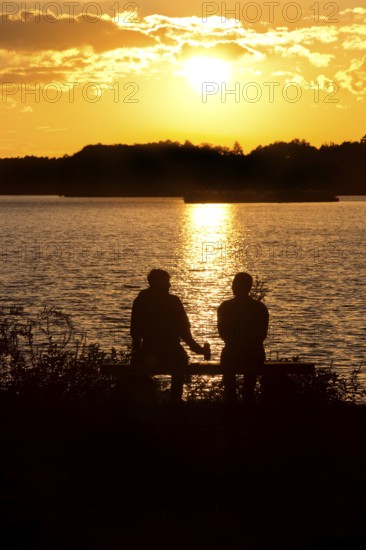 Two men sitting on a bench at sunset at Lake Gudelack, Lindow (Mark), Stechlin-Ruppiner Land nature park Park, Brandenburg, Germany