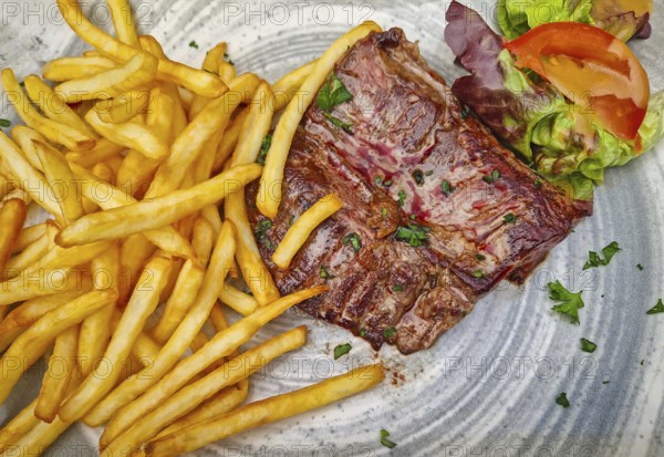 A large steak frites plate, featuring a well-seared skirt steak piled next to a generous portion of golden french fries. The meal is garnished with parsley and a simple salad of lettuce and tomato, Honfleur, Normandy, France