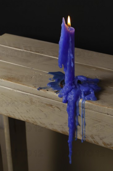 Blue candle lit and melted on a wooden table with a black background