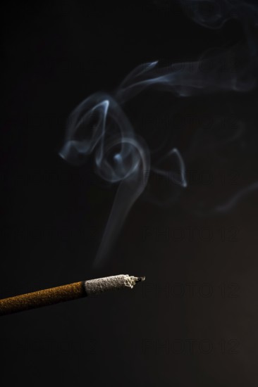 Close-up of a burning incense with white smoke coming out illuminated on a black background