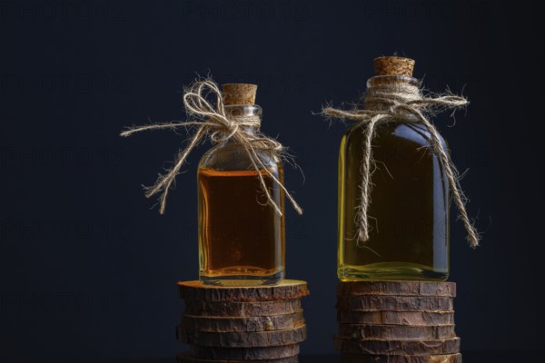 Close-up of two glass bottles with cork stopper and raffia string with rosemary oil and rose oil on a dark background