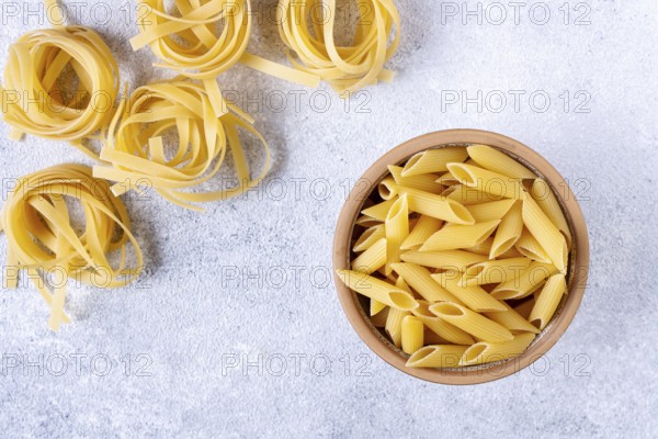 Tagliatelle and Penne on a light textured background, top view, space for text