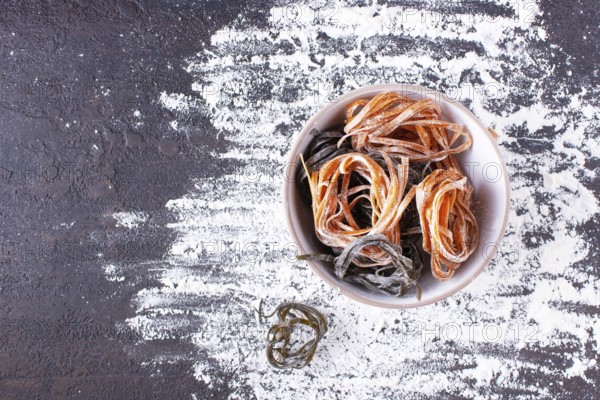Pasta with carrots and spinach in a round plate on a floured table, space for text
