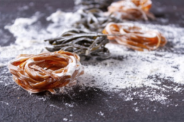 Pasta with carrots and spinach lies in a stack on a floured table, space for text
