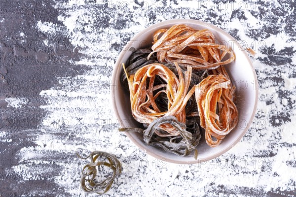 Pasta with carrots and spinach in a round plate on a table covered with flour, top view, space for text