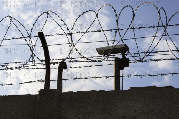 Security camera behind barbed wire fence stretched around prison walls Prague Czech republic