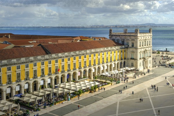 Scenic view of Commerce Square or Praca do Comercio in Lisbon, Portugal, iconic yellow Pombaline architecture, bustling outdoor cafes, Tagus River, city life, historic downtown, sunny day, sky with clouds. Sun ray over building, travel destination