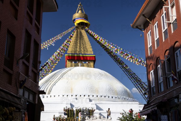 Boudhanath, the Boudha Stupa, the largest stupa in Nepal, Buddhist religious complex, UNESCO World Heritage Site and one of the main Kathmandu Valley tourist attractions. The upper part of the dome and the gilded, golden spire with Buddhist prayer flags stretched from the top. Eyes on the cubic part, the harmika, represent all-seeing, wisdom eyes of the Buddha. Seen in the afternoon on a clear, blue-sky, early autumn day. Kathmandu, Bagmati Province, Nepal