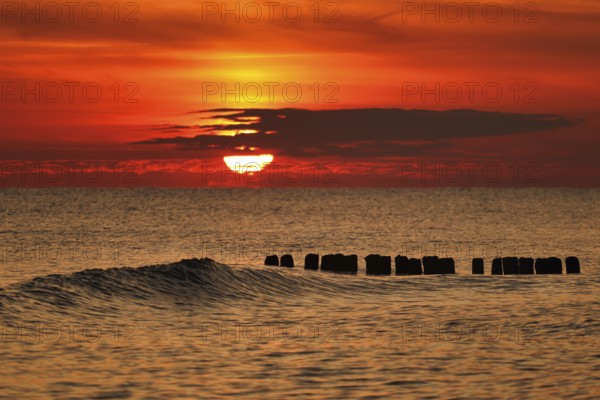 A vivid sunset over the sea with gentle waves and an orange sky creating a tranquil atmosphere. Baltic sea, Poland, Kolobrzeg