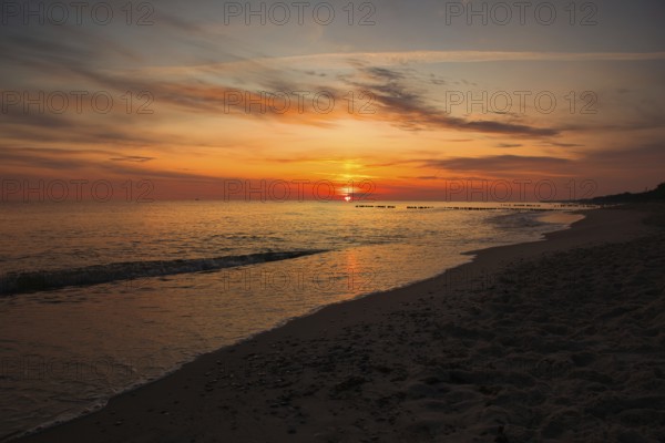 A serene sunset over the sea with golden skies and gentle waves lapping at the sandy beach. Sea Baltic, Poland, Kolobrzeg