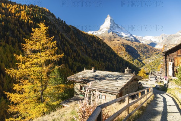 Matterhorn Mountain, Houses of Village, Wooden Path and Yellow Larches in Autumn in Sunny Morning. Fall Colors. Swiss Alps. Valais, Switzerland