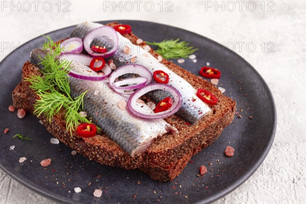 Sandwiches, herring fish, on dark rye bread, sprinkled with onion, chili pepper and herbs, on a dark plate