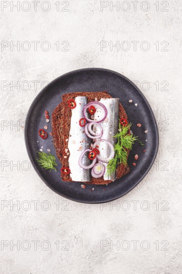 Sandwiches, herring fish, on dark rye bread, sprinkled with onion, chili pepper and herbs, on a dark plate