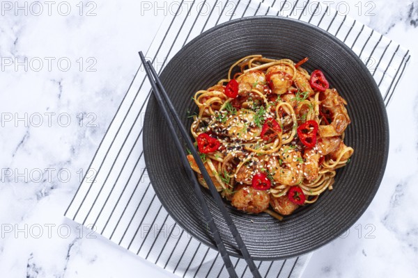 Delicious shrimp stir-fry with noodles and colorful vegetables served in a black bowl on a striped napkin