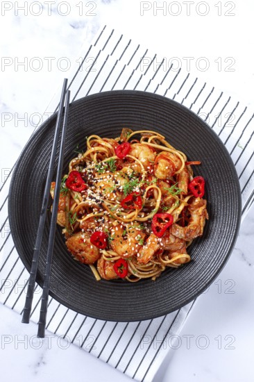 Delicious shrimp stir-fry with noodles and colorful vegetables served in a black bowl on a striped napkin