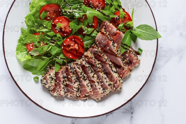 Fried tuna in sesame seeds, sliced on a plate, with fresh salad, on a white plate, homemade