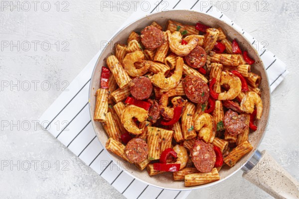 Jambalaya pasta with shrimp and sausages, cooked with bell pepper in a frying pan, homemade, on a marble kitchen countertop