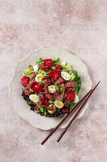 Salad with fresh tuna, cherry tomatoes and quail eggs and avacado, served with chopsticks