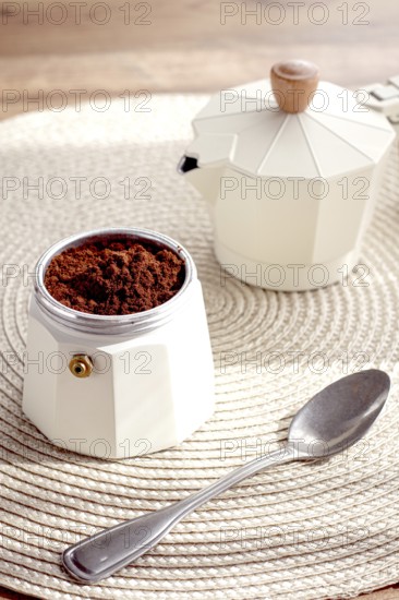 Geyser coffee maker with ground coffee and a spoon on the background of a woven rug, coffee preparation, natural light, breakfast