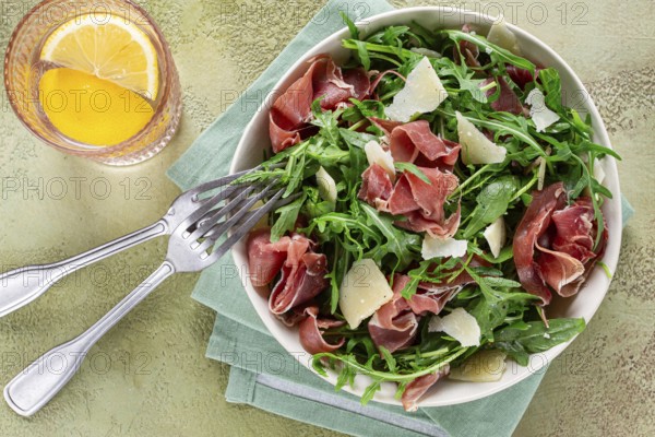 Fresh arugula salad with prosciutto and grated parmesan cheese, on a plate, homemade, no people