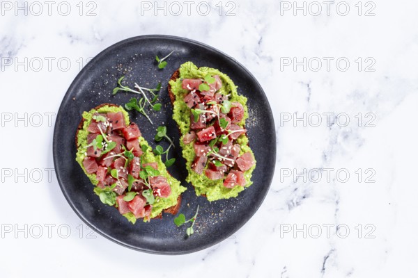 Fresh tuna tartare on avocado spread toast with microgreens served on a black plate