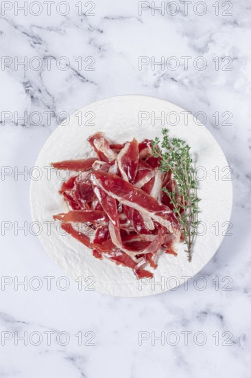 Ham of duck breast, dried duck fillet, with a sprig of thyme, white plate, on a marble table
