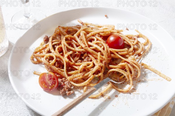 A plate holds freshly cooked spaghetti topped with flavorful meat sauce and garnished with bright cherry tomatoes. A glass sits nearby, reflecting a relaxed dining atmosphere