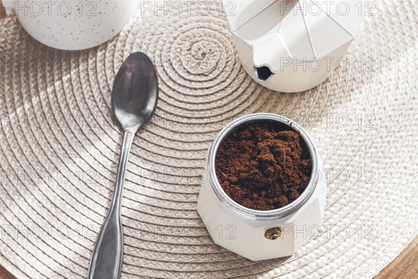 Geyser coffee maker with ground coffee and a spoon on the background of a woven rug, coffee preparation, natural light, breakfast
