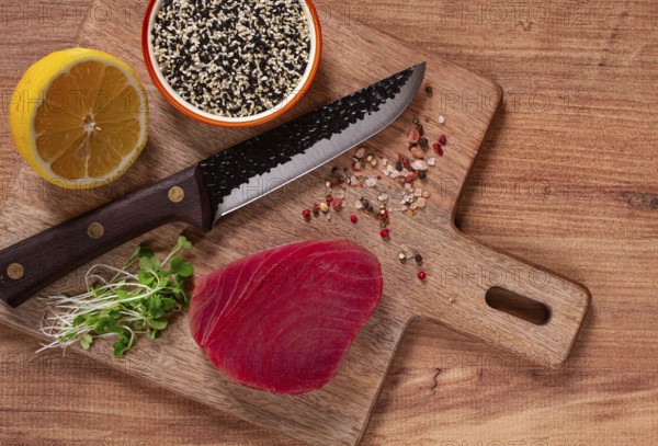 Fresh tuna steak, on a wooden cutting board, with lemon and sesame seeds, on a wooden table