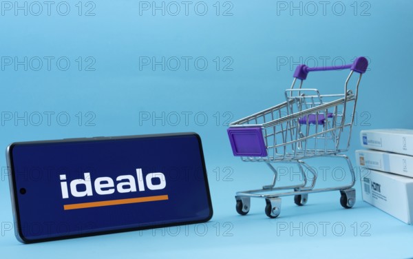 Dhaka, Bangladesh- 03 July 2025: Smartphone with idealo logo next to a small shopping cart and boxes against a blue background