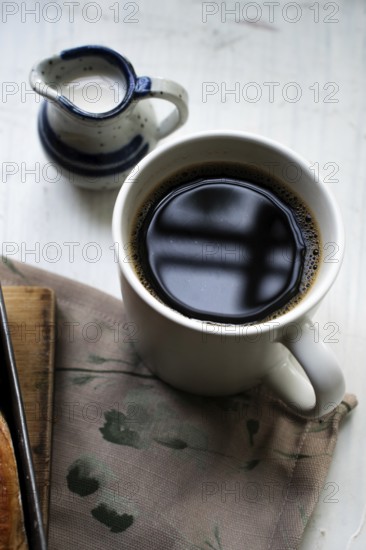 A cup of black coffee with a small pot of milk